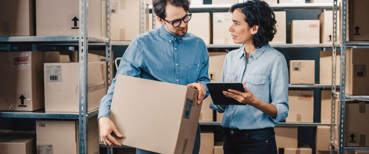 An inventory manager and her associate stand amid shelves of boxes prepared for shipment.