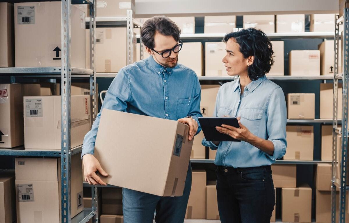 An inventory manager and her associate stand amid shelves of boxes prepared for shipment.