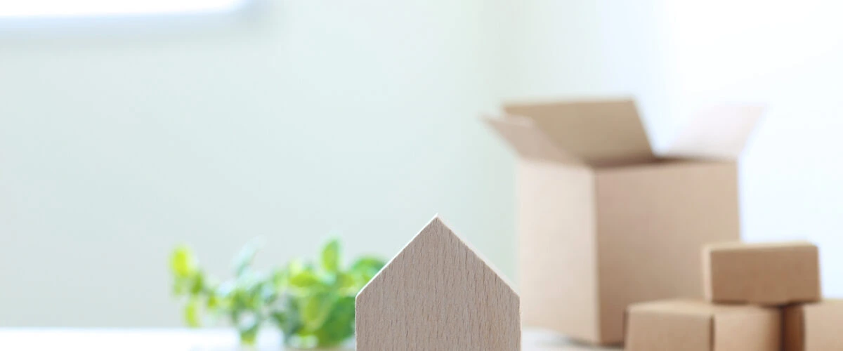 A house-shaped wooden block with moving boxes in the background.