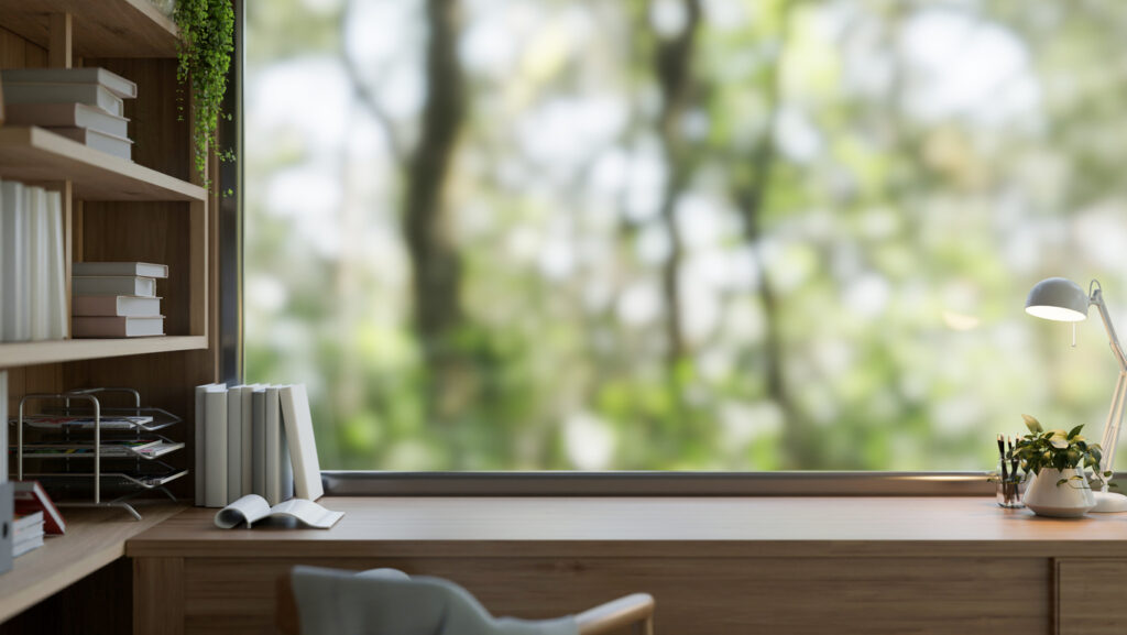 An uncluttered desk in front of a large window in an organized home office.