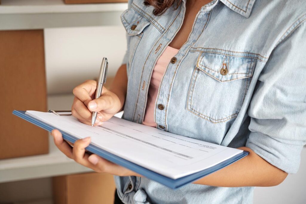 A person reviewing a rental agreement on a clipboard with a pen in hand at a storage office.