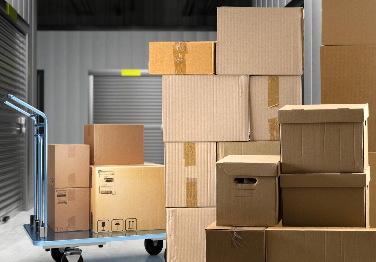 Several boxes sitting outside a storage unit on the floor or on a dolly.