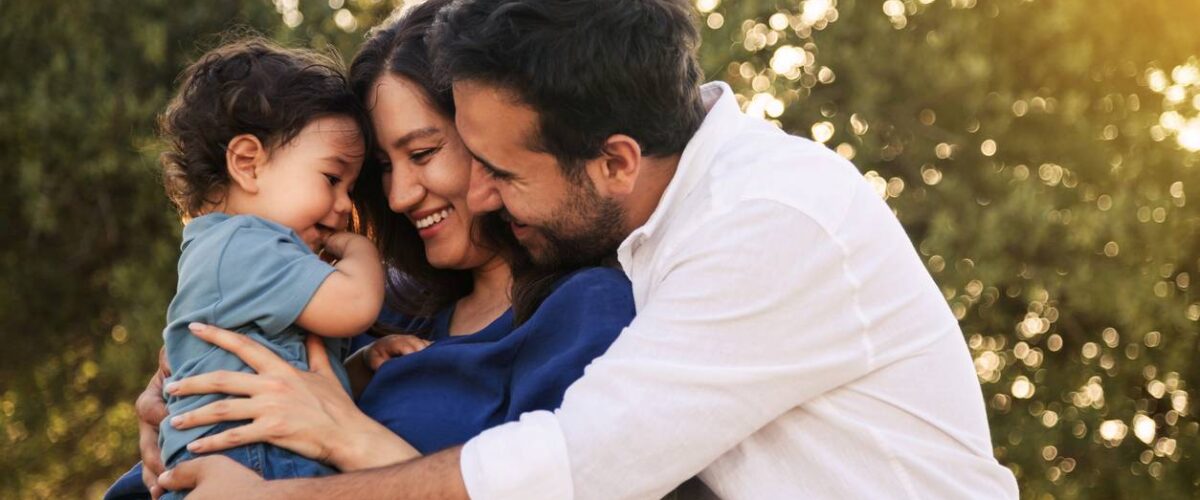 A young couple holds their baby and enjoys time together in their yard.