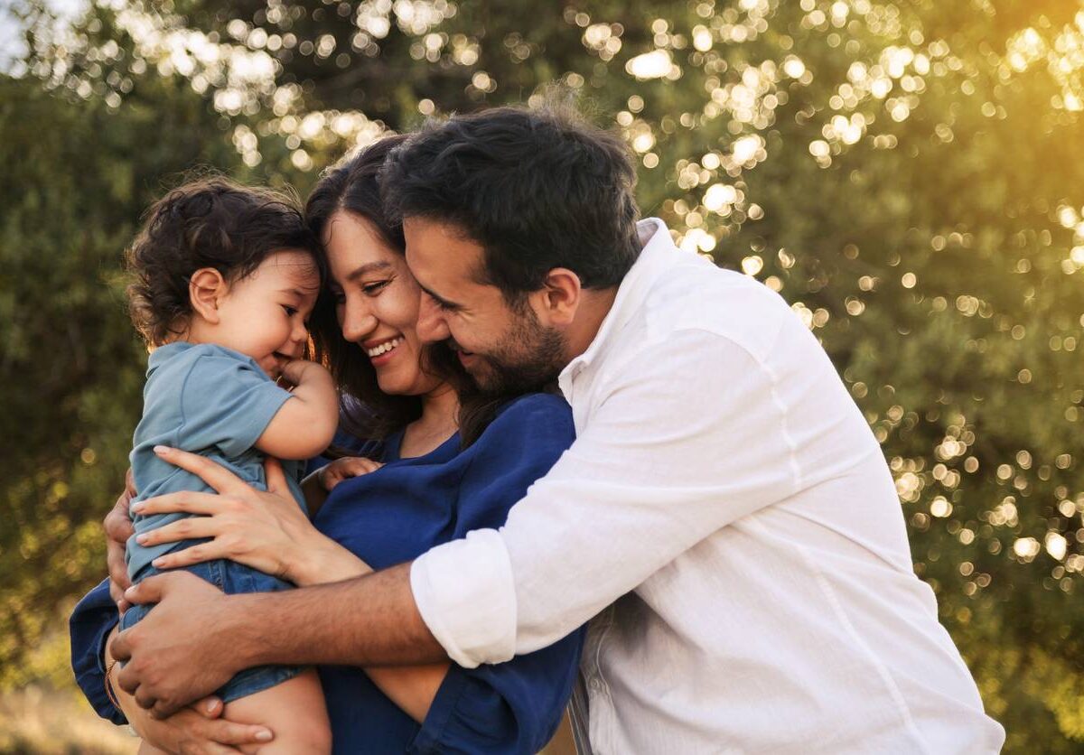 A young couple holds their baby and enjoys time together in their yard.