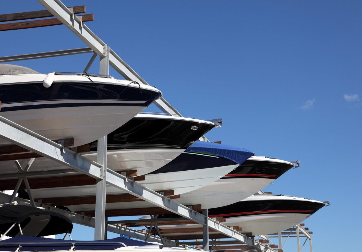 Several different colored boats are placed on an outdoor storage rack at a facility.