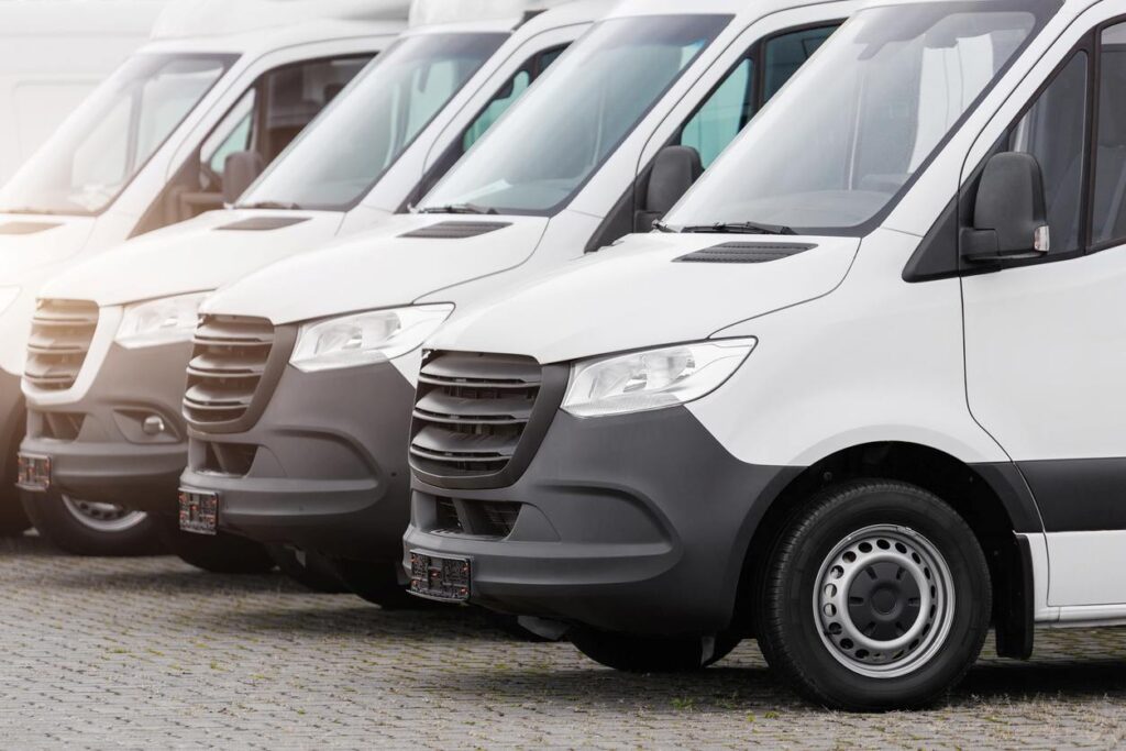 Several white and black-colored vans are parked in a row in an outdoor lot.
