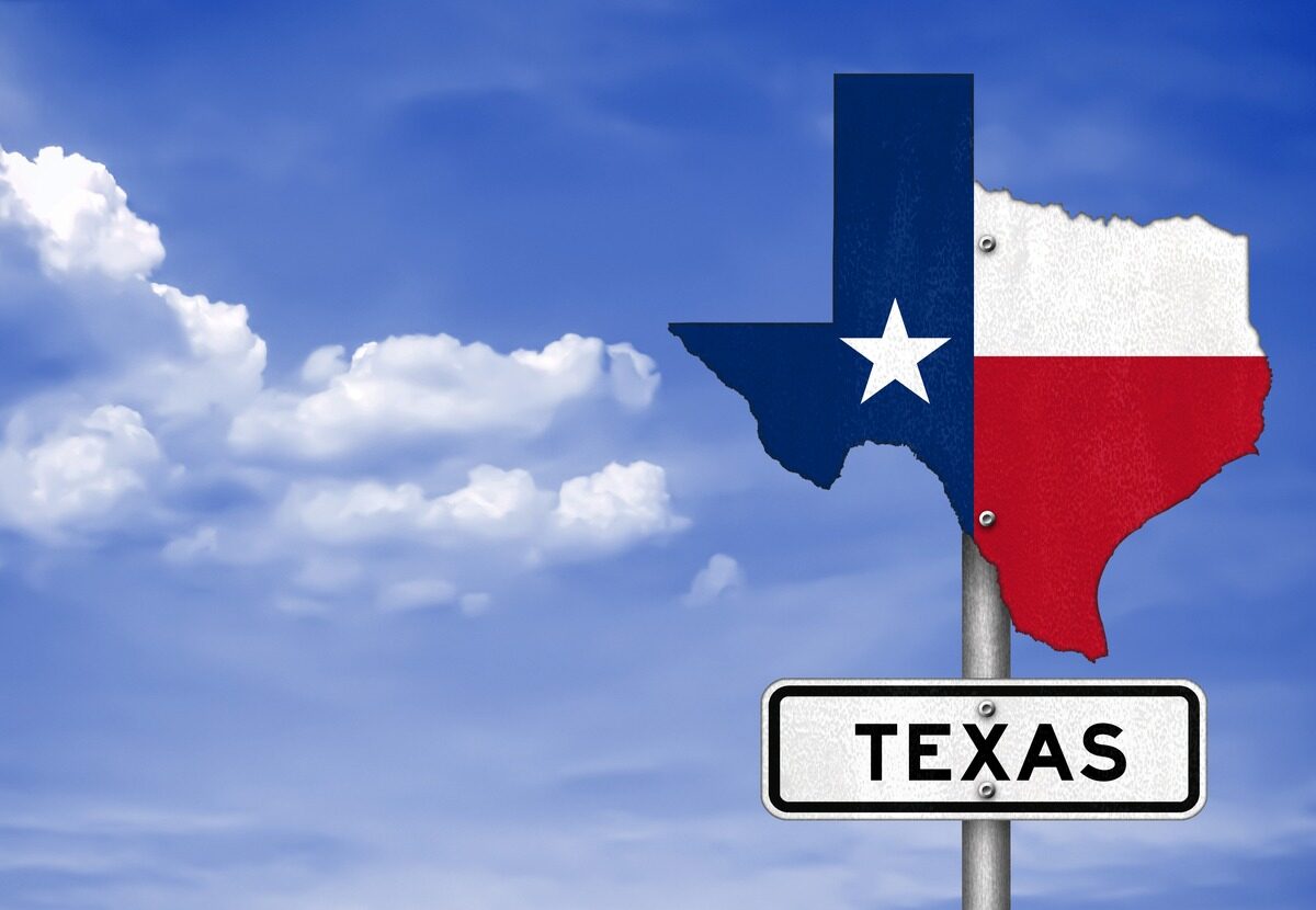 A road sign labeled “Texas” with an accompanying sign shaped like the state against a blue sky.